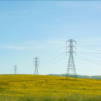 High-tension lines cut across rolling hills, weaving a modern energy network amidst the natural landscape.